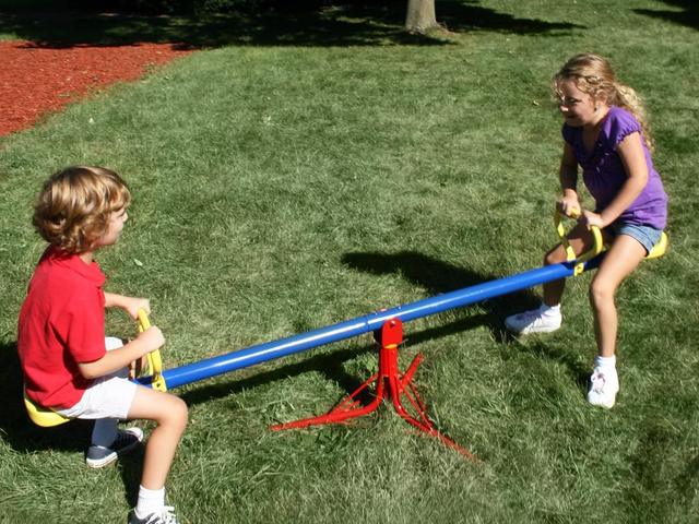 Children riding a blue spinning see saw on the grass